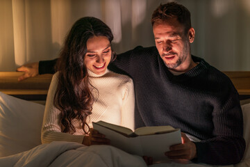 caucasian couple lying on bed reading book in bedroom together