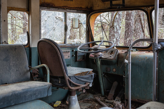 Driver's seat in an abandoned decaying school bus with broken windows