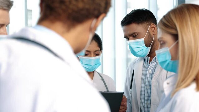 Multiracial team of doctors discussing a patient standing grouped in the foyer looking at a tablet, close up. Diverse multiracial medical team consulting on a patient records grouped around a tablet