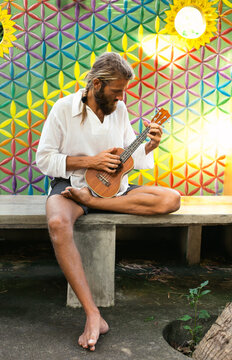 Hippie man playing ukulele in front of colorful flower of life wall