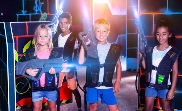 Modern teenage girl and boys with laser guns playing laser tag on dark arena. High quality photo © JackF