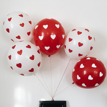 White and red balloons with hearts on them hanging from wooden frame.
