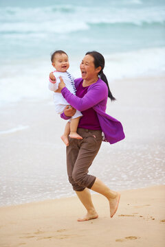 happy asian senior woman holding her granddaughter on beach