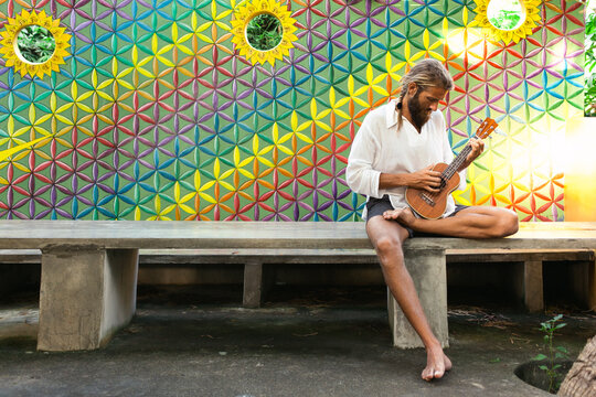 Hippie man playing ukulele in front of colorful flower of life wall