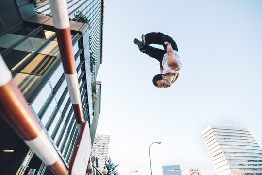 man doing a backflip in the air over a barrier during a parkour training in a city