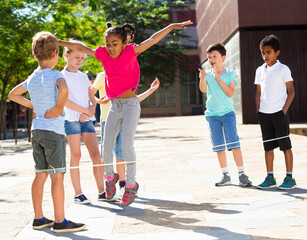 Energetic kids playing and skipping on elastic jumping rope in european yard. High quality photo