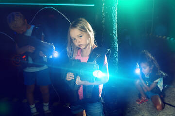Portrait of teenager girl with laser gun having fun on dark lasertag arena. High quality photo