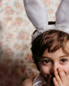Child playfully smiling, wearing bunny ears, and hiding his mouth with his hands