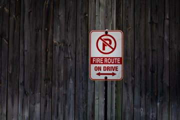 A vertical and rectangle shaped no parking sign signifying a fire route is tacked up to a weathered wooden fence in London, Ontario, Canada, February 2021.  