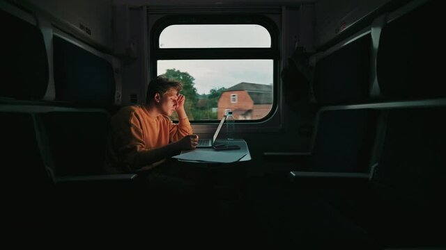 Positive young man working at a table in a train on the road on a laptop. Work in a compartment train.