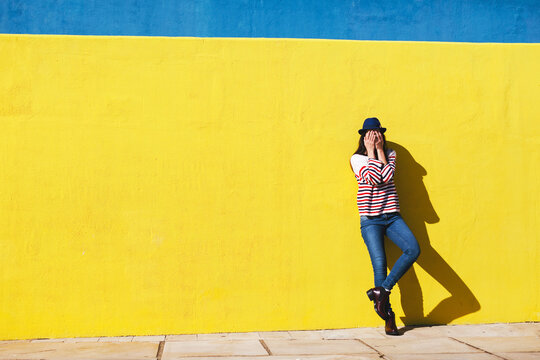 Young woman hiding her face in front of yellow background.