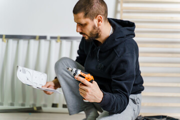 One Man with beard alone Putting Together Self Assembly Furniture sitting on the floor at Home...