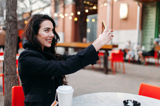 Young Woman Drinking Coffee with her Cellphone at a Cafe