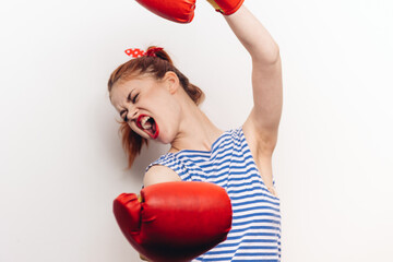 aggressive sportswoman in boxing gloves and a striped t-shirt fights on a light background