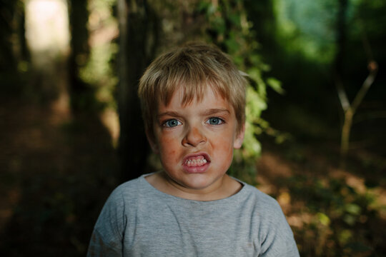 Boy covered in red clay dust bares his teeth while pretending to be a tiger in a forest.