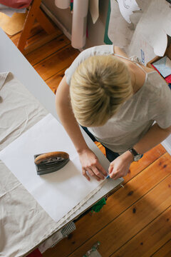 Overhead Shot of Blond Female Designer Marking Fabric in Bright Dressmaking Workshop