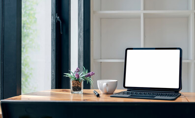 Mockup blank screen tablet with magic keyboard on wooden table in cafe.