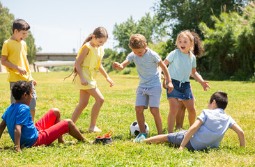 Fototapeta premium Group of happy schoolchildren playing football together in park