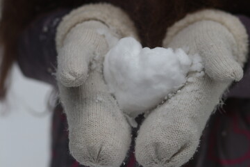 A heart-shaped snowball is kept in mittens