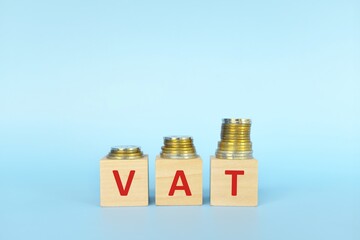 VAT letters on wooden blocks in blue background increasing stack of coins. Increase on value added tax concept.