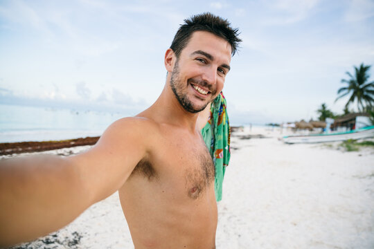 Young man taking a selfie in a tropical beach at sunset