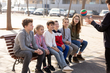 Group of cheerful children relaxing on bench on playground, playing with ball. High quality photo