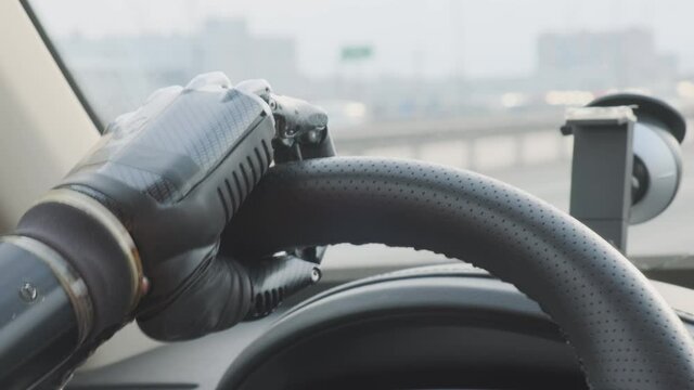 Man robot drives car while driving along road, artificial hand on steering wheel of car close-up.