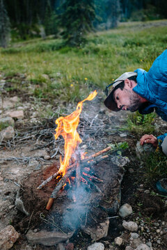 Man feeding sticks to small fire outdoors while camping