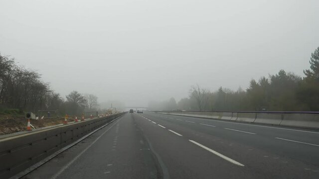 Car windshield view driving motorway M1 southbound in the United Kingdom on a misty overcast morning or day.