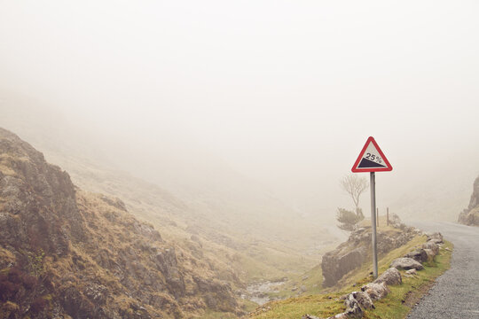 A foggy mountain road with road sign warning of a steep road ahead