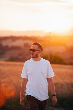 Man in sunglasses looking to one side as he walks in the countryside a golden hour