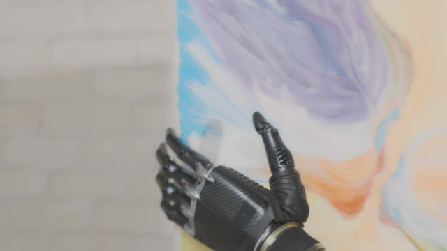 Talented artist woman disabled with bionic prosthetic arm hangs picture on wall in studio.