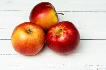 Three red ripe apples on white wooden table.
