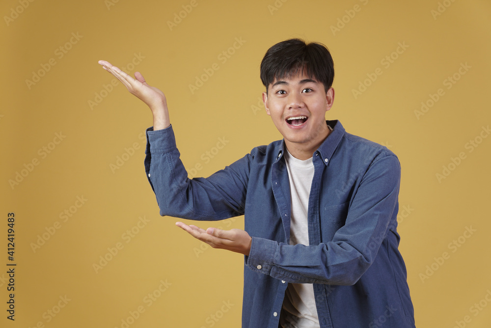 Wall mural portrait of happy handsome young asian man dressed casually presenting with open palms gesture at co