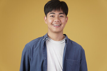 portrait of smiling happy cheerful young asian man dressed casually. yellow background
