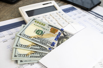 Dollars in a white envelope lie on a business document against the background of a white calculator. Business and financial concept