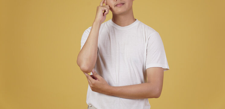 Portrait Of Thoughtful Young Asian Man Dressed Casually Thinking Doubting Wondering Isolated On Yellow Background