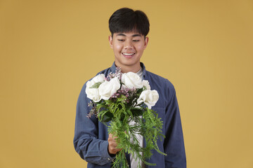 smiling happy cheerful young asian man dressed casually holding flower bouquet isolated on yellow background.