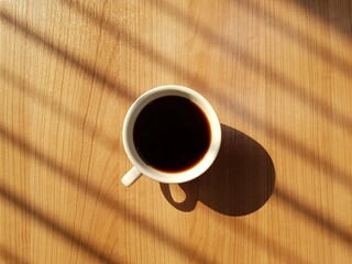 A cup of coffee on wooden table with warm natural light.