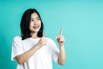 Young elegant Asian woman smiling and pointing to empty copy space isolated on blue background