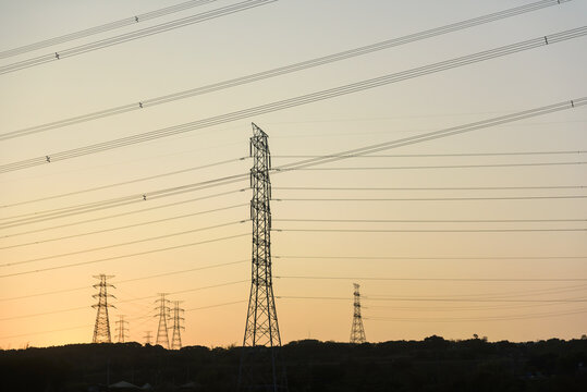 high voltage electricity cables silhouetted against a colorful orange sunset sky