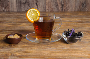 Cup of tea, sugar, lemon and tea leaves on a wooden table.