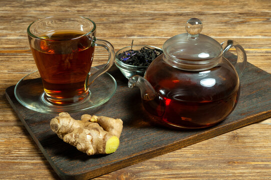 Glass cup of tea with saucer, teapot, tea leaves and dinger on wooden table. Close-up