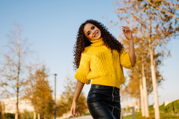 A very cute smile on the face of a curly beauty in a bright yellow sweater posing in an autumn...