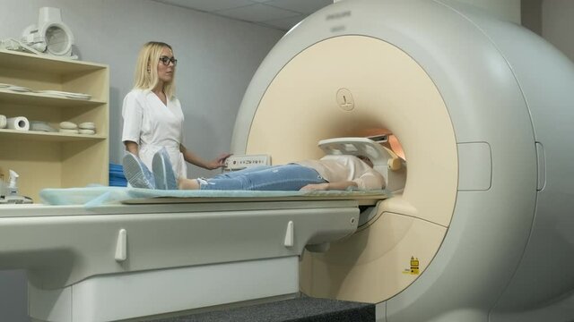 Woman doctor radiologist makes brain, head, neck MRI scanning. Young female patient on automatic table leaves closed-type mri machine using modern equipment, coil on the patient's head.