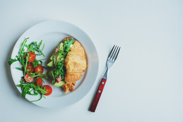 healthy tasty breakfast - croissant with avocado, arugula, ham and cheese served with cherry tomato salad on white plate
