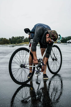 Hip young man fixed his bike in the rain