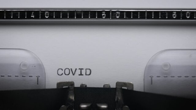 Typing text COVID on vintage manual typewriter. Close up of writes word on white paper. Shot in macro 4K resolution. Concept of Coronavirus.