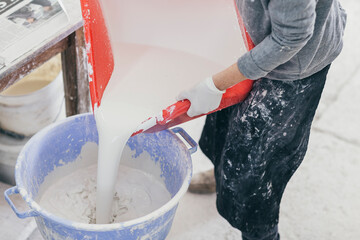 Person mixing white glazing paint in a bucket