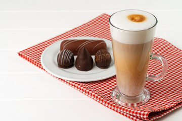 Cup of coffee and saucer with chocolate sweets on wooden table